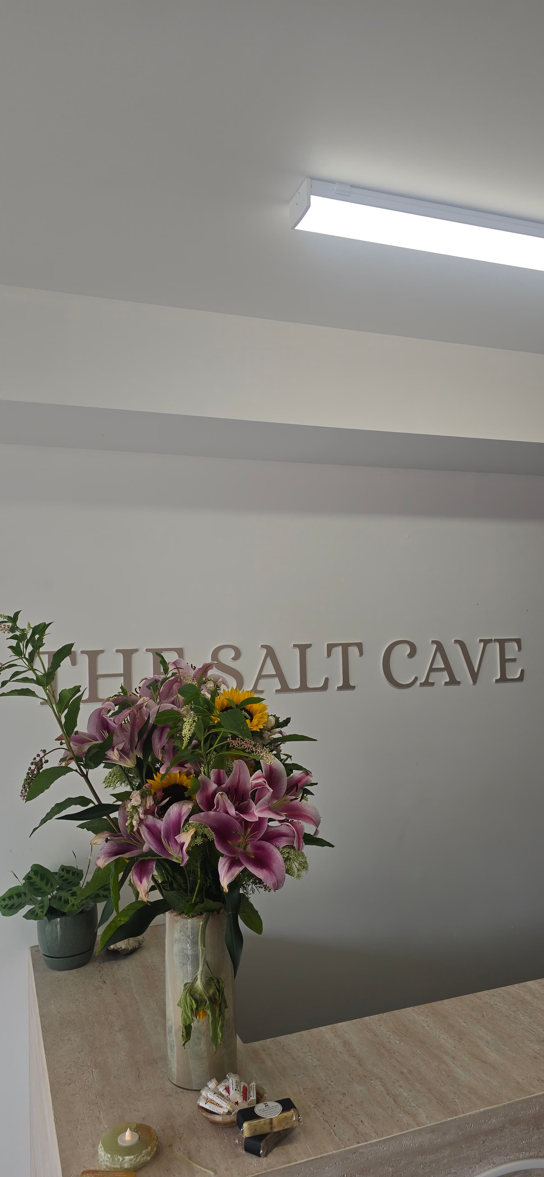 Bouquet of pink lilies and sunflowers on a counter below THE SALT CAVE wall sign.