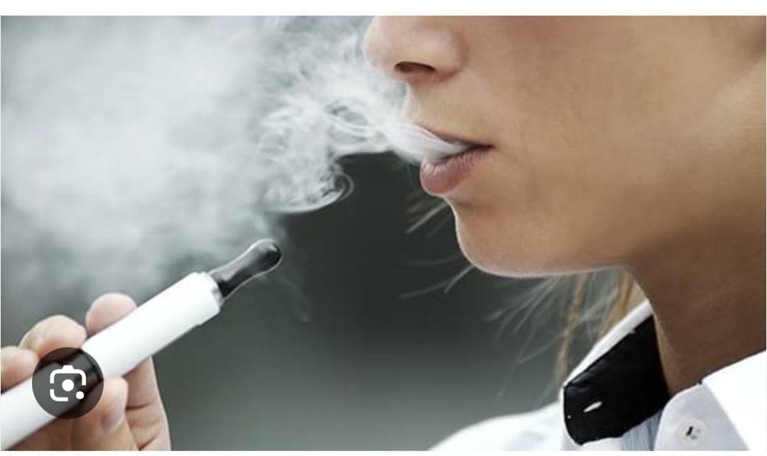 Close-up of a person exhaling white vapor while holding a white electronic cigarette.