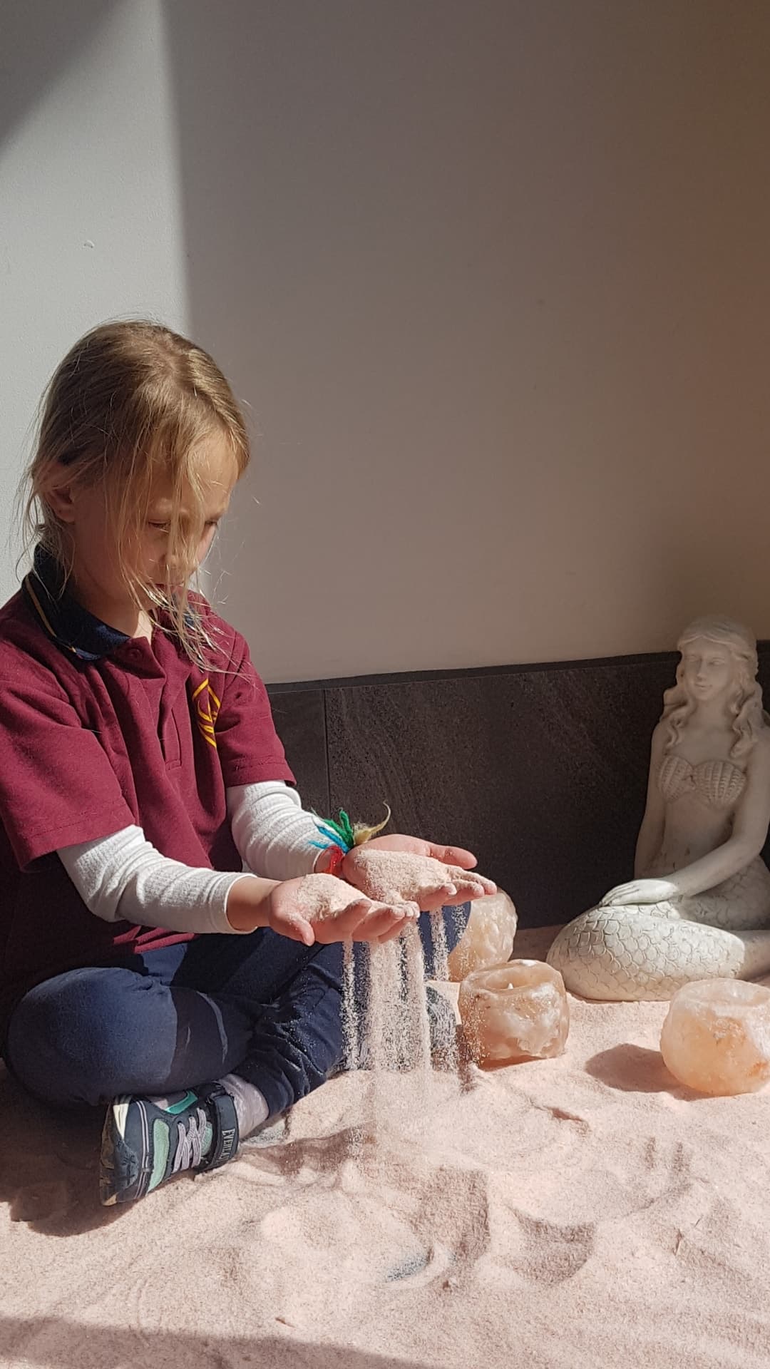 Young girl pours pink salt through her hands while sitting near a white mermaid statue.